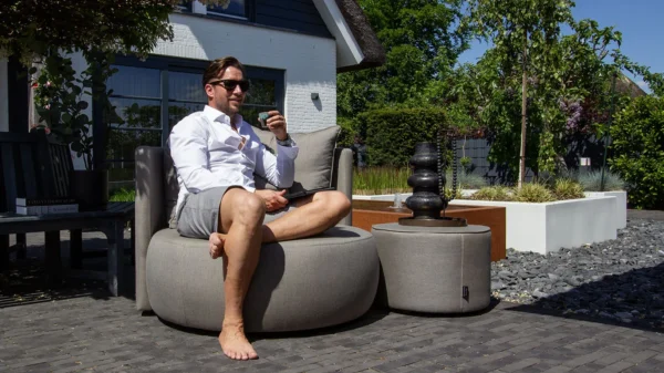 UrbanSofa Outdoor Fauteuil Venice in Natte Grey Chine met Swing Functie en Bellagio Outdoor Poef low in Natte Grey Chine kop koffie drinken in de Tuin